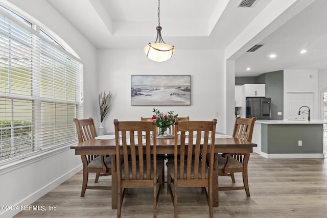 dining area with plenty of natural light, a tray ceiling, and light hardwood / wood-style floors