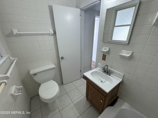 bathroom with tile walls, tile patterned flooring, vanity, a tub to relax in, and toilet