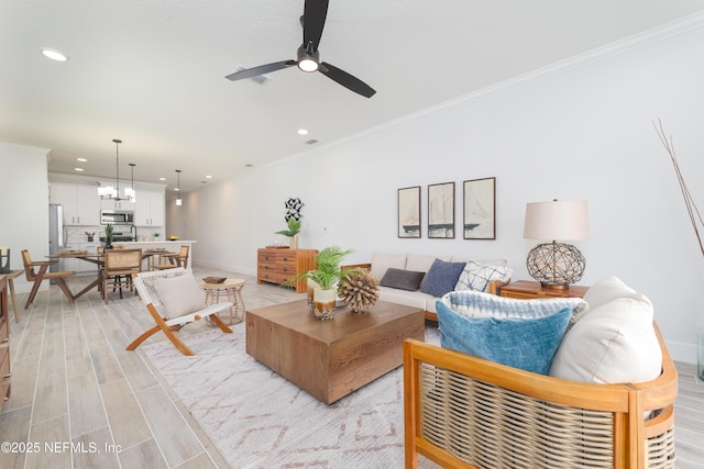 living room with ceiling fan with notable chandelier, ornamental molding, and light hardwood / wood-style floors