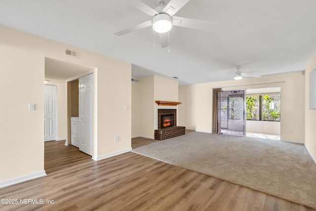 unfurnished living room with ceiling fan, a brick fireplace, and light wood-type flooring