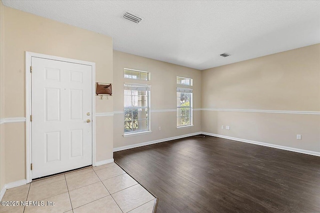 foyer entrance with light wood-style floors, baseboards, visible vents, and a textured ceiling