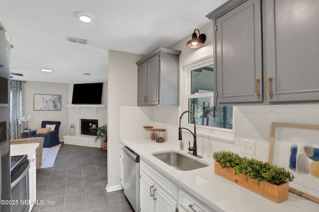 kitchen featuring a fireplace, dishwasher, sink, gray cabinetry, and backsplash