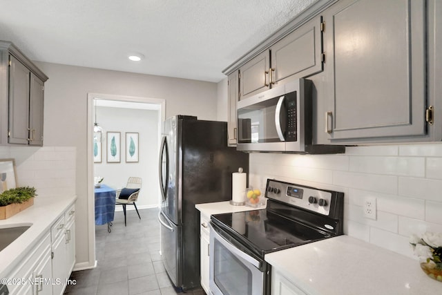 kitchen with light tile patterned flooring, appliances with stainless steel finishes, gray cabinetry, and decorative backsplash