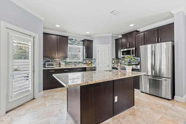 kitchen featuring an island with sink, dark brown cabinetry, appliances with stainless steel finishes, and light stone countertops