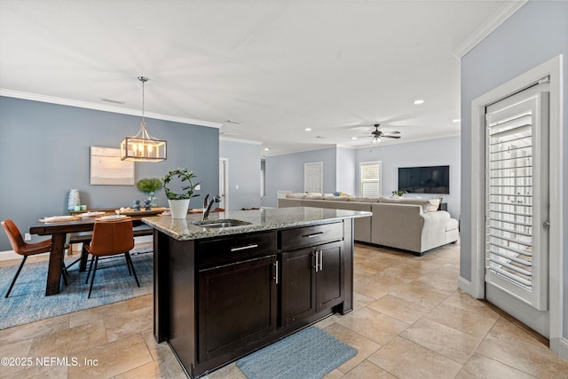 kitchen with pendant lighting, open floor plan, a kitchen island with sink, a sink, and light stone countertops