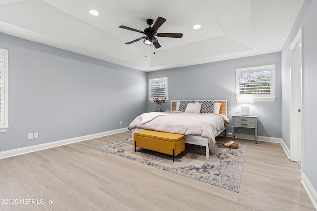 bedroom with light wood-type flooring, a raised ceiling, baseboards, and recessed lighting