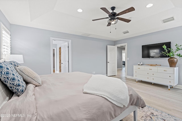 bedroom with visible vents, a tray ceiling, light wood-style flooring, and baseboards