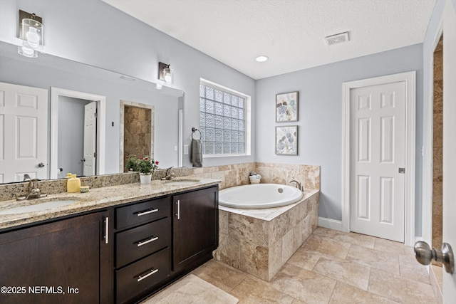 bathroom with double vanity, visible vents, a sink, a textured ceiling, and a bath