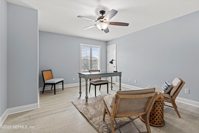 home office featuring light wood-style floors, a textured ceiling, baseboards, and a ceiling fan