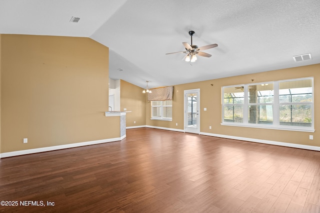 unfurnished living room featuring ceiling fan with notable chandelier, wood finished floors, visible vents, baseboards, and vaulted ceiling