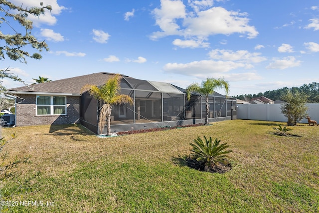 rear view of house featuring glass enclosure, a yard, brick siding, and fence