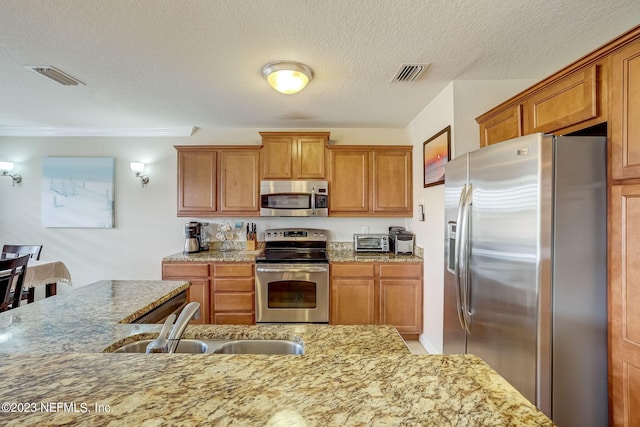 kitchen with light stone counters, stainless steel appliances, sink, and a textured ceiling