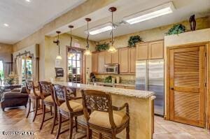 kitchen with a breakfast bar, hanging light fixtures, light brown cabinets, appliances with stainless steel finishes, and kitchen peninsula