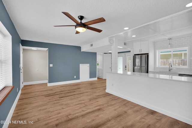 unfurnished living room featuring ceiling fan, sink, a textured ceiling, and light wood-type flooring