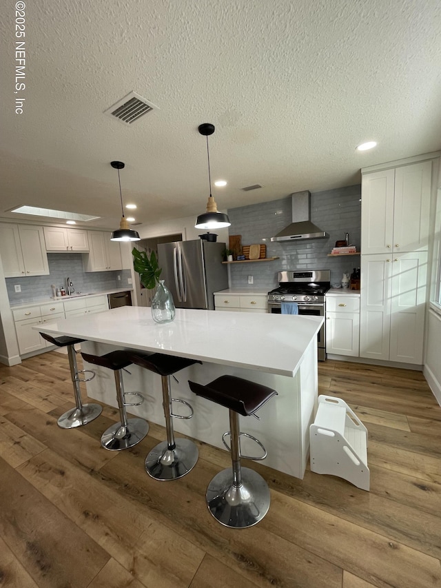 kitchen with pendant lighting, stainless steel appliances, a spacious island, light countertops, and wall chimney range hood