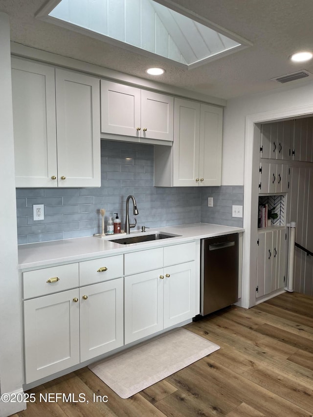 kitchen featuring white cabinets, black dishwasher, light countertops, and a sink