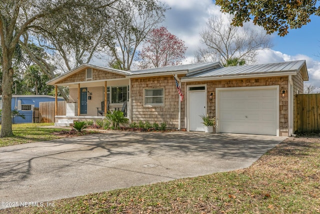 ranch-style home featuring covered porch, fence, metal roof, a garage, and driveway