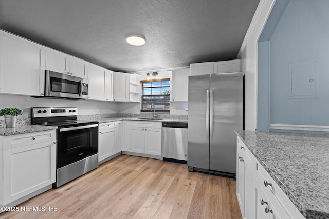 kitchen with appliances with stainless steel finishes, white cabinetry, sink, light hardwood / wood-style floors, and a textured ceiling