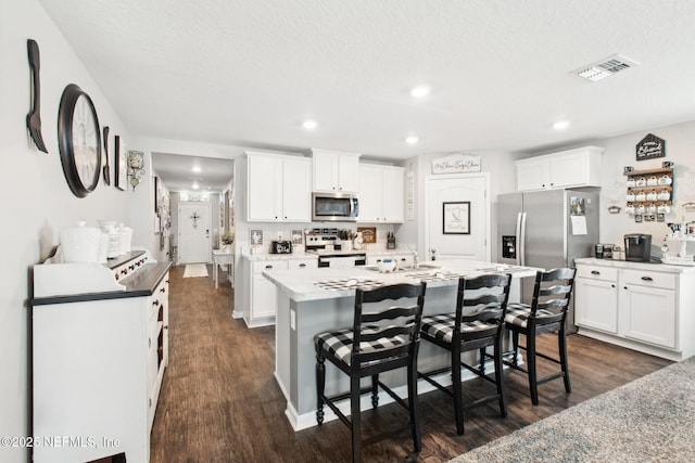 kitchen with dark wood-type flooring, appliances with stainless steel finishes, an island with sink, and white cabinets