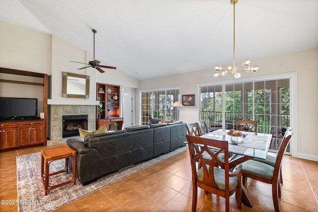 tiled dining area featuring ceiling fan with notable chandelier, a fireplace, and high vaulted ceiling