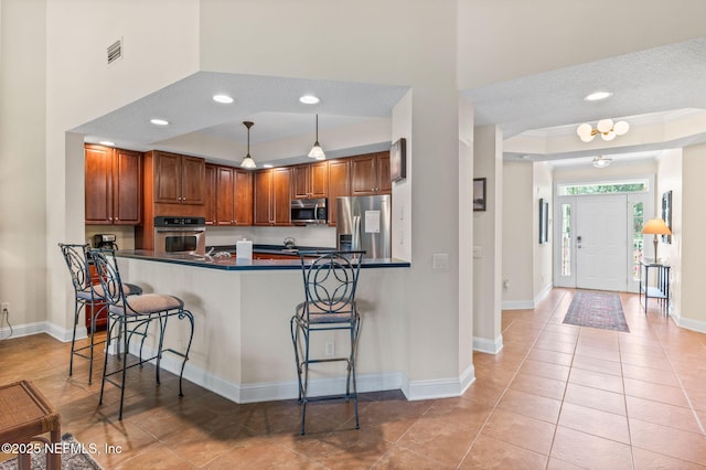 kitchen featuring appliances with stainless steel finishes, decorative light fixtures, kitchen peninsula, and a kitchen bar