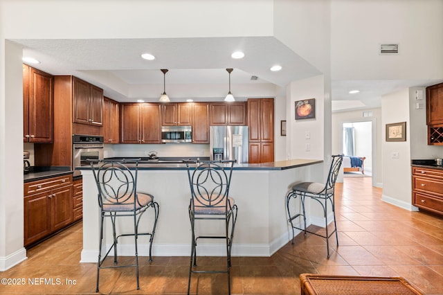 kitchen featuring a raised ceiling, a kitchen bar, hanging light fixtures, tile patterned flooring, and stainless steel appliances