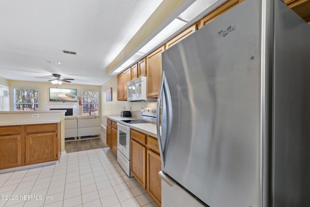 kitchen with white appliances, a textured ceiling, light tile patterned floors, ceiling fan, and a tiled fireplace