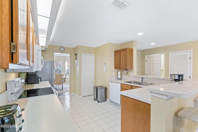 kitchen with light tile patterned flooring, sink, a textured ceiling, kitchen peninsula, and white appliances