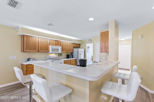 kitchen with a kitchen breakfast bar, hardwood / wood-style flooring, white appliances, and kitchen peninsula