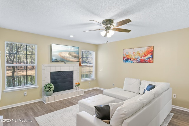 living room featuring ceiling fan, wood-type flooring, a tile fireplace, and a textured ceiling