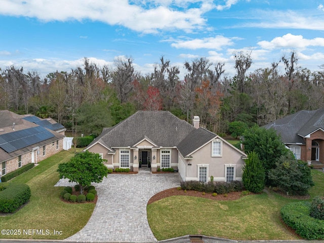 view of front of property featuring a chimney, decorative driveway, a front yard, and stucco siding