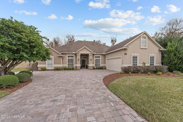 view of front of property with a garage, a front yard, decorative driveway, and stucco siding