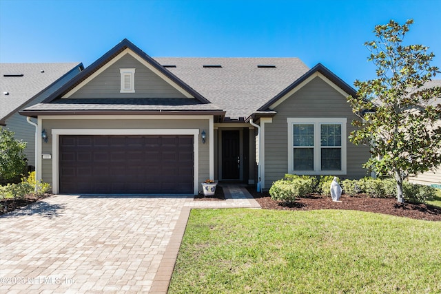 view of front facade featuring roof with shingles, a front lawn, decorative driveway, and an attached garage