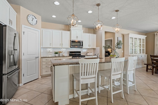 kitchen featuring decorative backsplash, appliances with stainless steel finishes, white cabinetry, dark stone countertops, and an island with sink