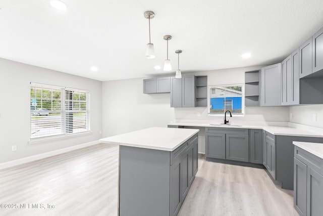 kitchen featuring light wood finished floors, open shelves, gray cabinets, a kitchen island, and a sink