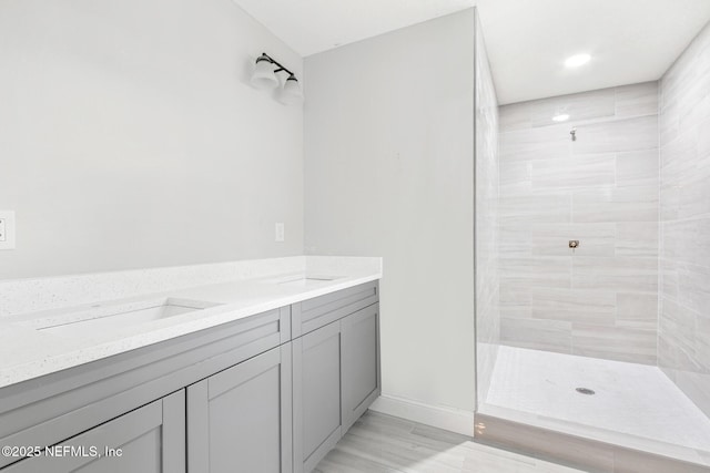 full bathroom featuring tiled shower, a sink, baseboards, and double vanity