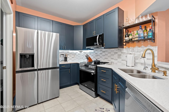 kitchen with blue cabinetry, light countertops, decorative backsplash, appliances with stainless steel finishes, and a sink