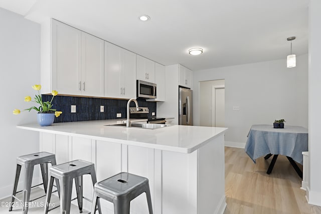 kitchen featuring stainless steel appliances, a peninsula, a kitchen breakfast bar, hanging light fixtures, and light countertops