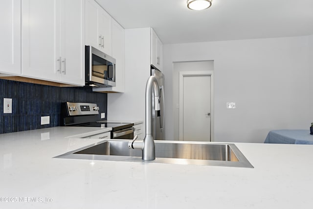 kitchen with stainless steel appliances, white cabinets, a sink, and tasteful backsplash