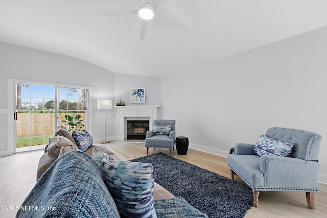 living area featuring lofted ceiling, a fireplace with flush hearth, a ceiling fan, wood finished floors, and baseboards