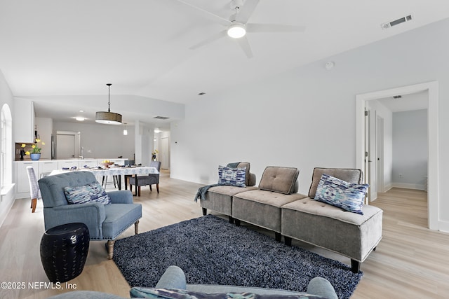 living room featuring visible vents, light wood-style flooring, vaulted ceiling, ceiling fan, and baseboards