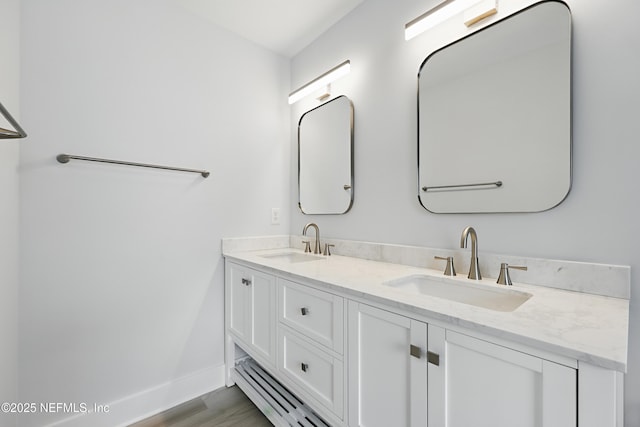 bathroom with double vanity, baseboards, a sink, and wood finished floors