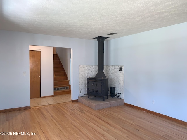 unfurnished living room featuring a wood stove, a textured ceiling, and light hardwood / wood-style flooring