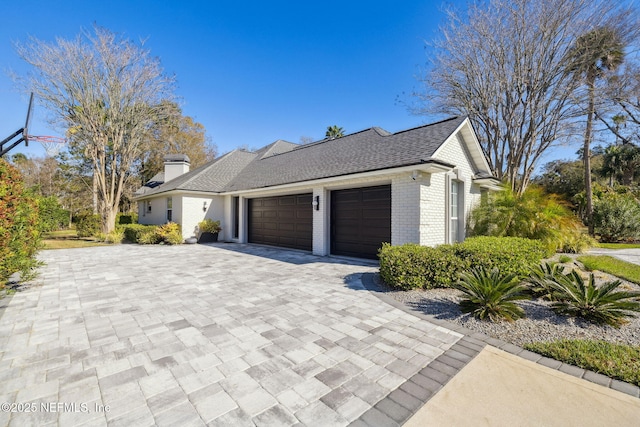 view of property exterior featuring a chimney, roof with shingles, an attached garage, decorative driveway, and brick siding