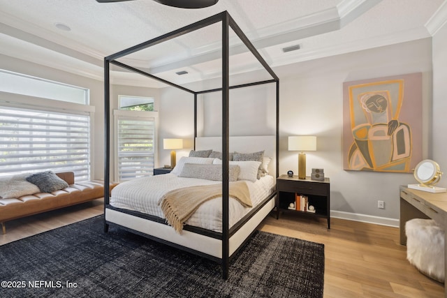 bedroom featuring baseboards, visible vents, light wood-style flooring, a tray ceiling, and crown molding