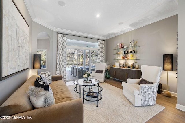 living area featuring arched walkways, ornamental molding, light wood-style flooring, and baseboards