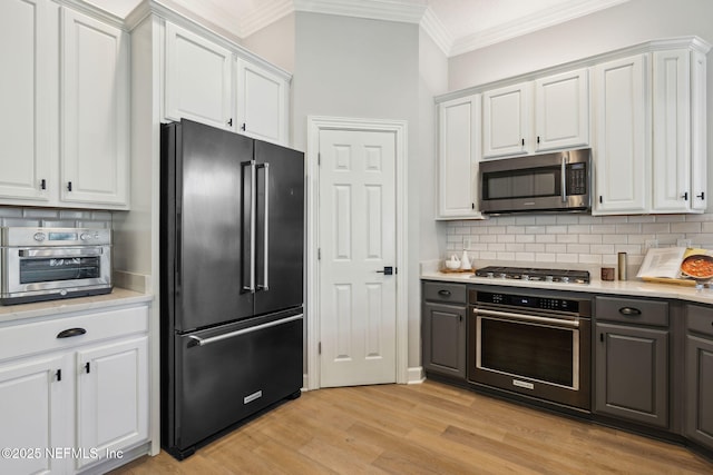 kitchen featuring white cabinets, light wood-style flooring, ornamental molding, stainless steel appliances, and light countertops