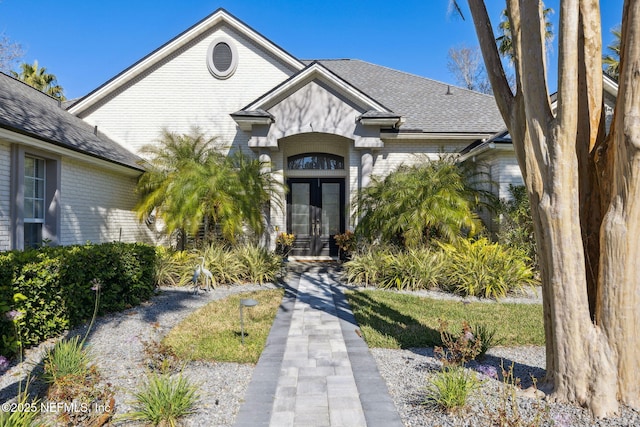 view of front of property featuring french doors, roof with shingles, and brick siding