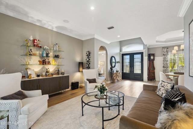 living area with light wood-type flooring, visible vents, crown molding, and french doors