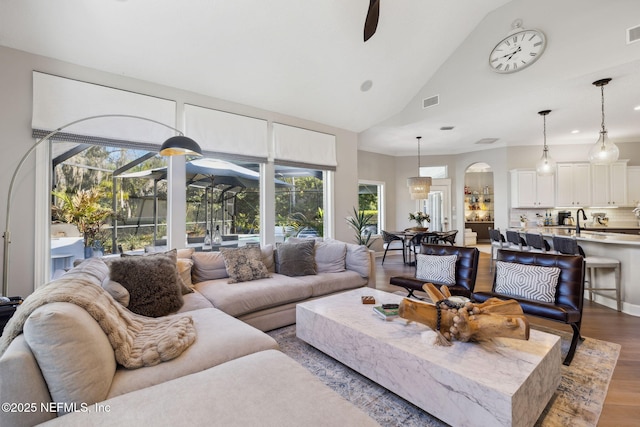 living area featuring ceiling fan, high vaulted ceiling, wood finished floors, visible vents, and a sunroom